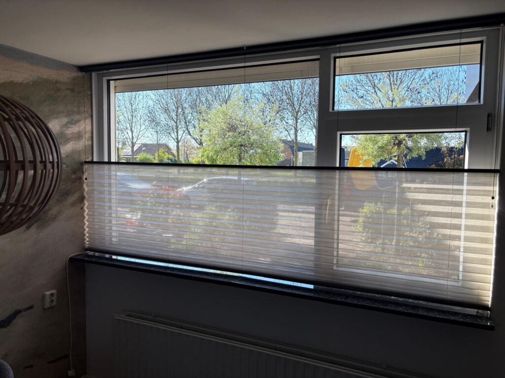 Door een raam met half gesloten jaloezieën valt zonlicht naar binnen.